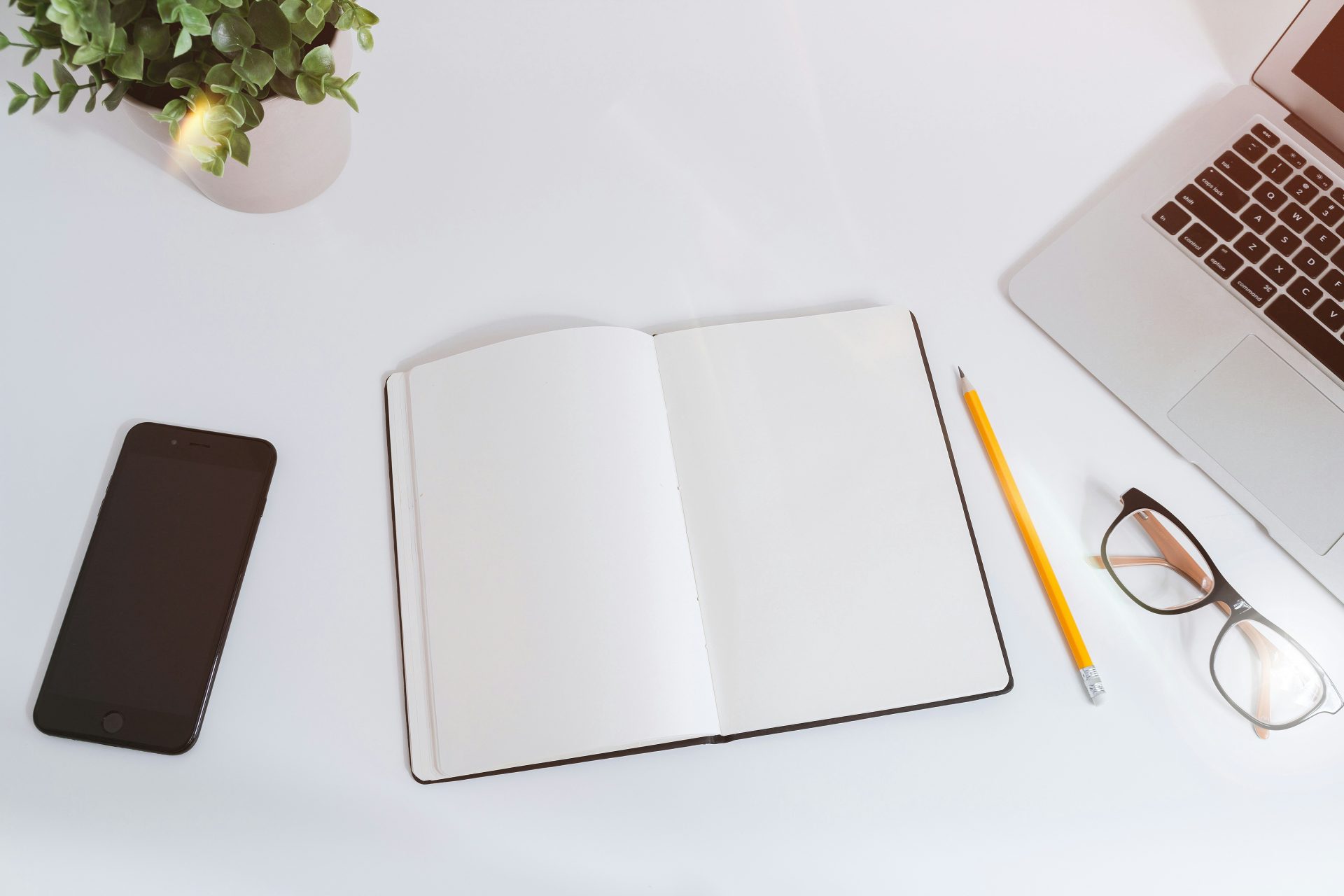 Un carnet vide et ouvert sur un bureau blanc, à côté d'un iPhone et d'un MacBook.